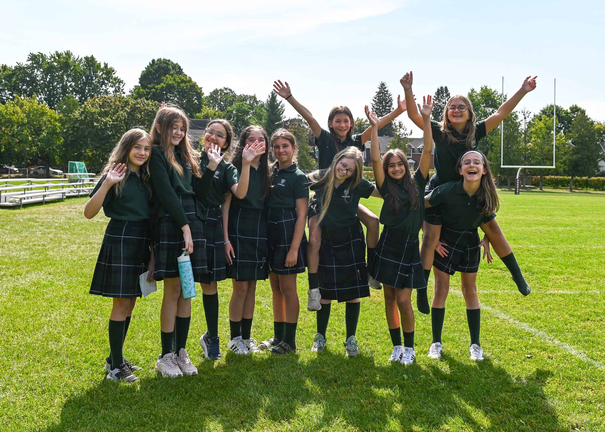 Group of young girls in green uniforms smiling and waving while on the field