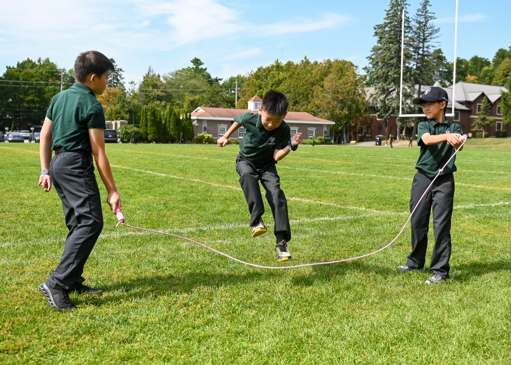 3 young boys playing with a jump rope on the field. 