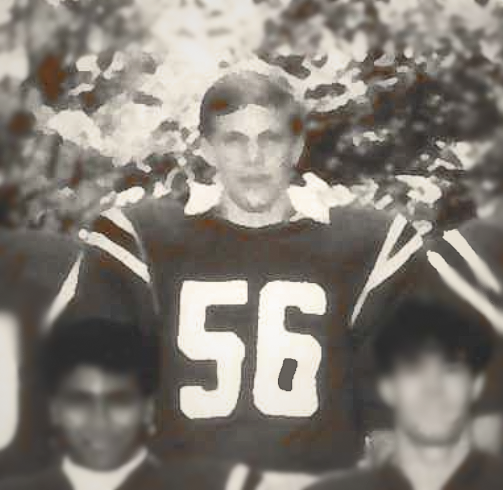 Vintage black-and-white photo of a football player wearing jersey number 56, standing outdoors with teammates and a serious expression.