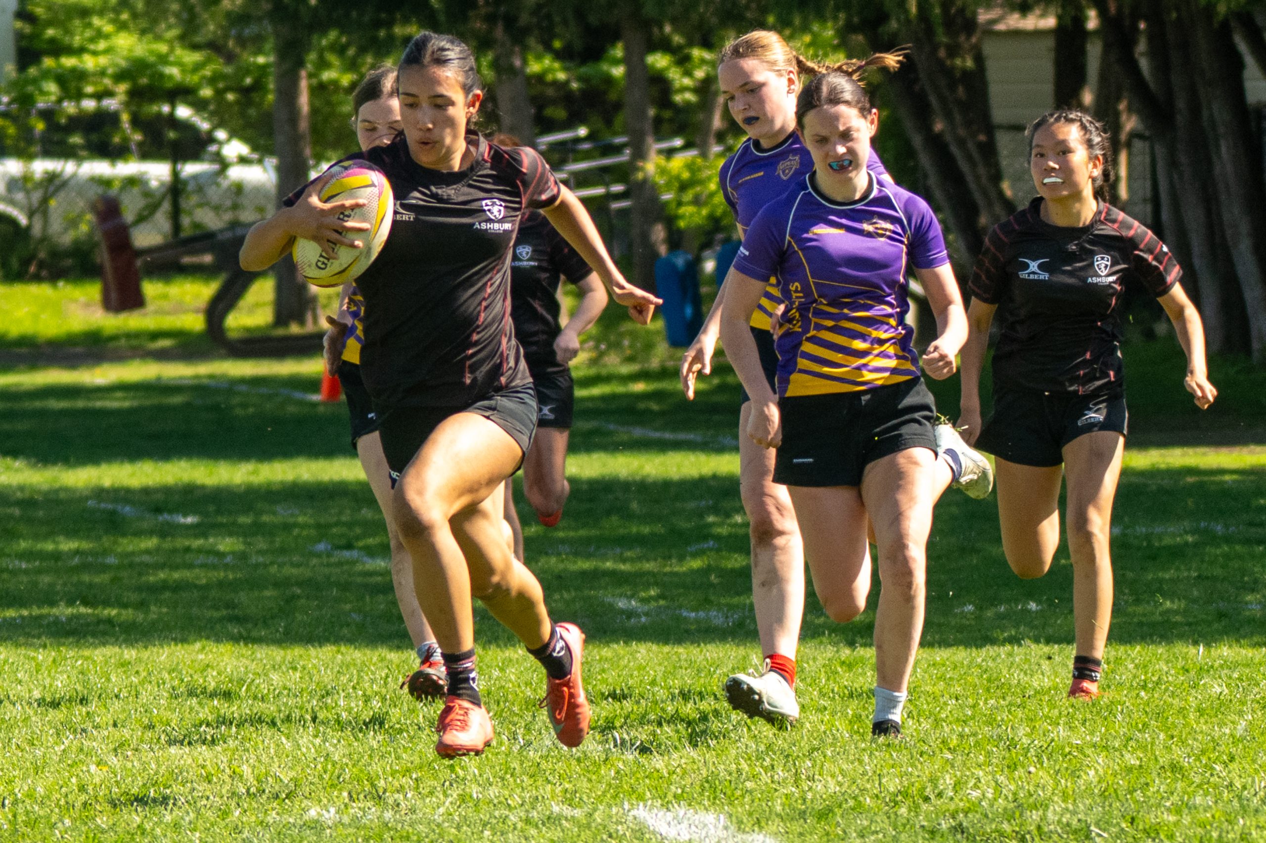 Woman in a rugby uniform sprinting ahead of the field with a rugby ball