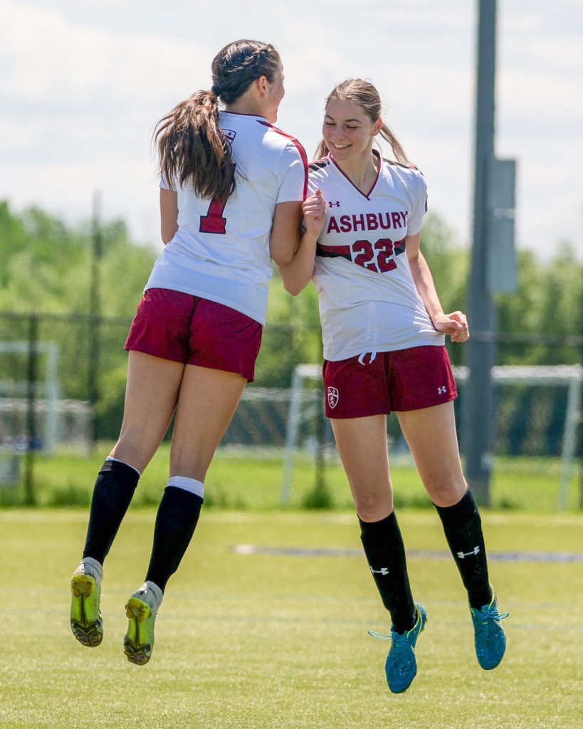 2 younger girls in soccer jerseys happily bumping shoulders and celebrating
